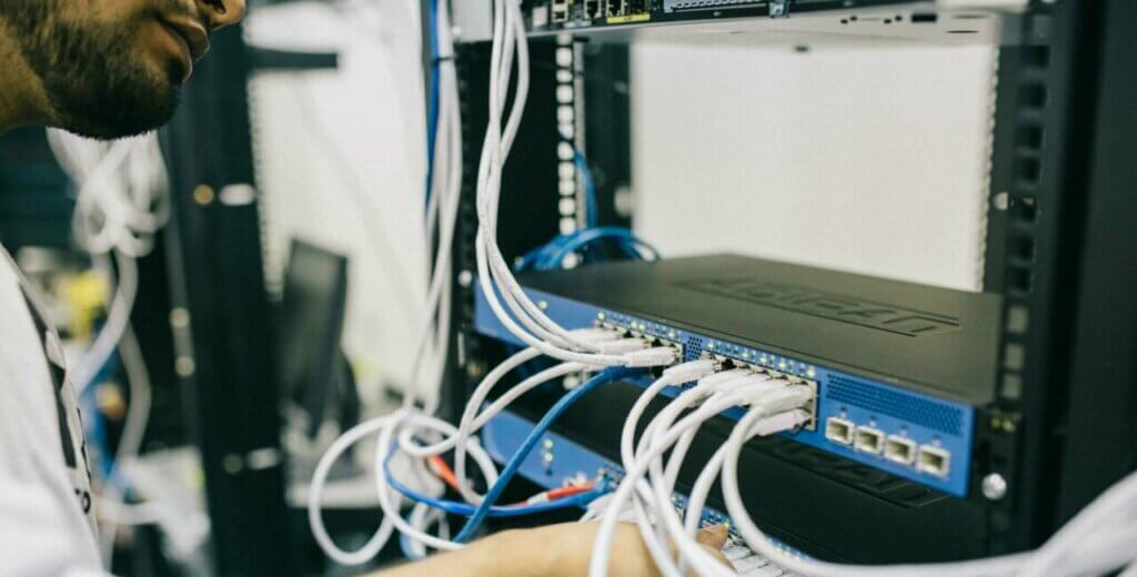 An IT professional configuring network cables in a server rack, focusing on Ethernet connections.